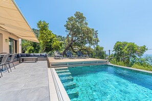 A swimming pool with a sun terrace, lounge chairs, and a large tree. - Villa sea view  (Rayol-Canadel-sur-Mer)