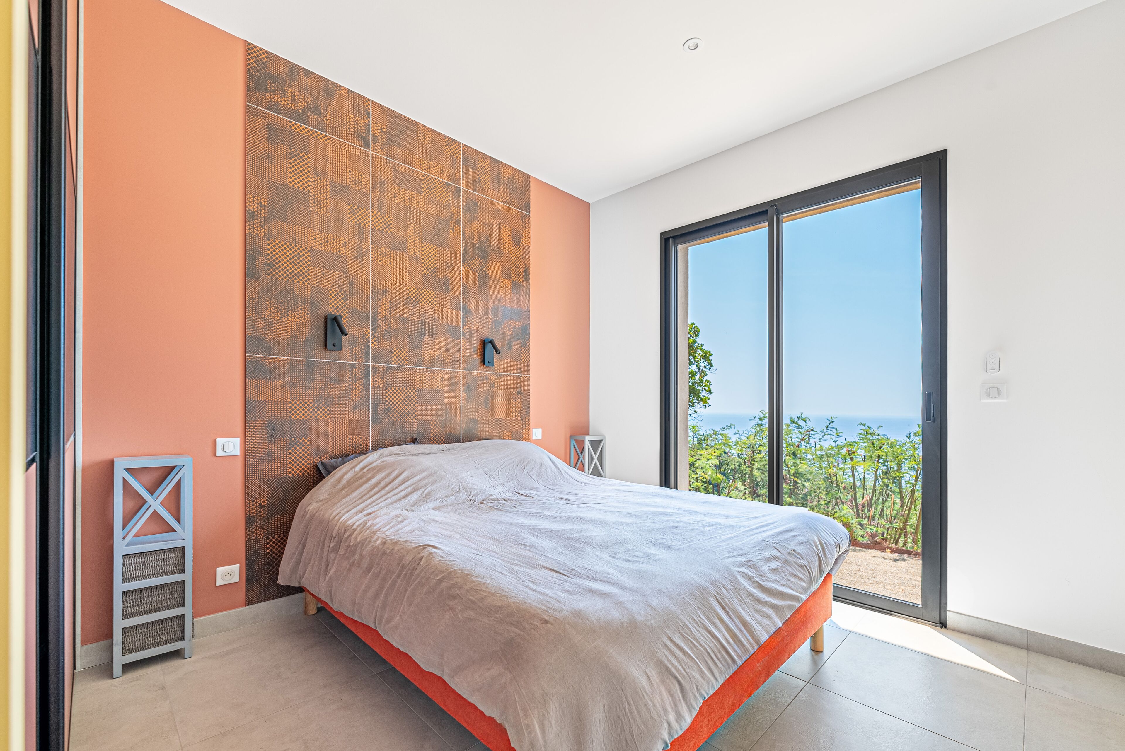 A modern bedroom with a large bed, a patterned wall, and a view of the outdoors.