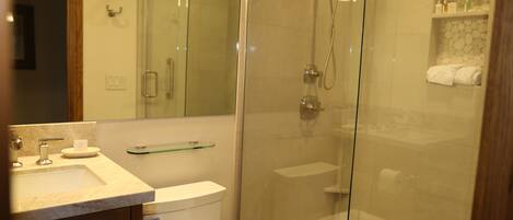 Un baño moderno con ducha de vidrio, lavamanos de mármol y un inodoro.