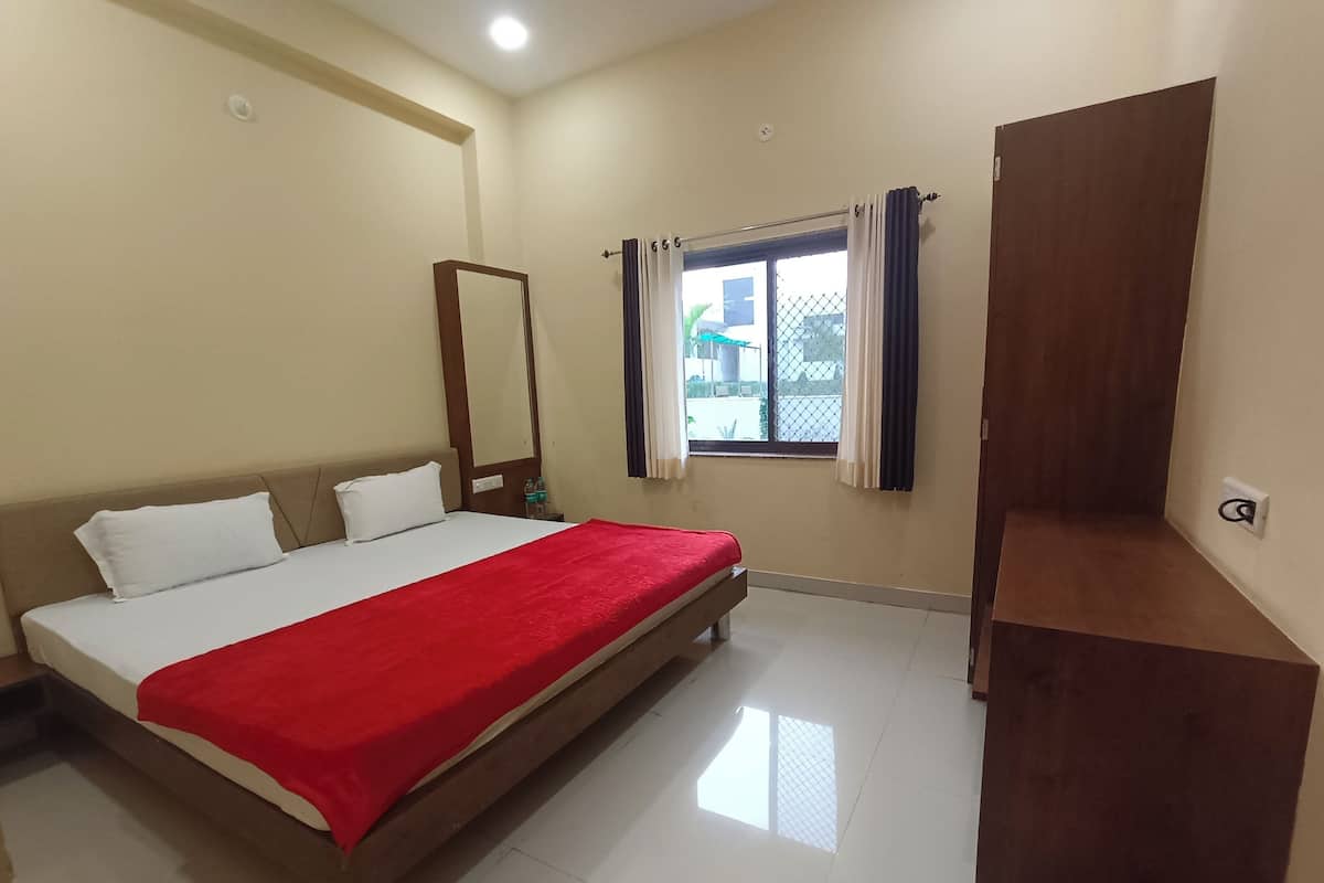 A bedroom with a bed, a window with curtains, a wooden wardrobe, and a mirror on the wall.
