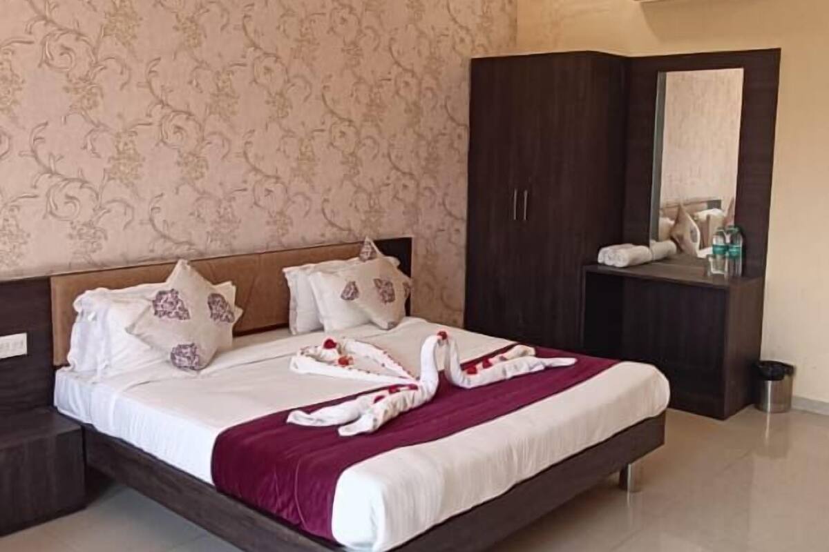 A hotel room with a bed, a wardrobe, a vanity with a mirror, and an air conditioning unit.
