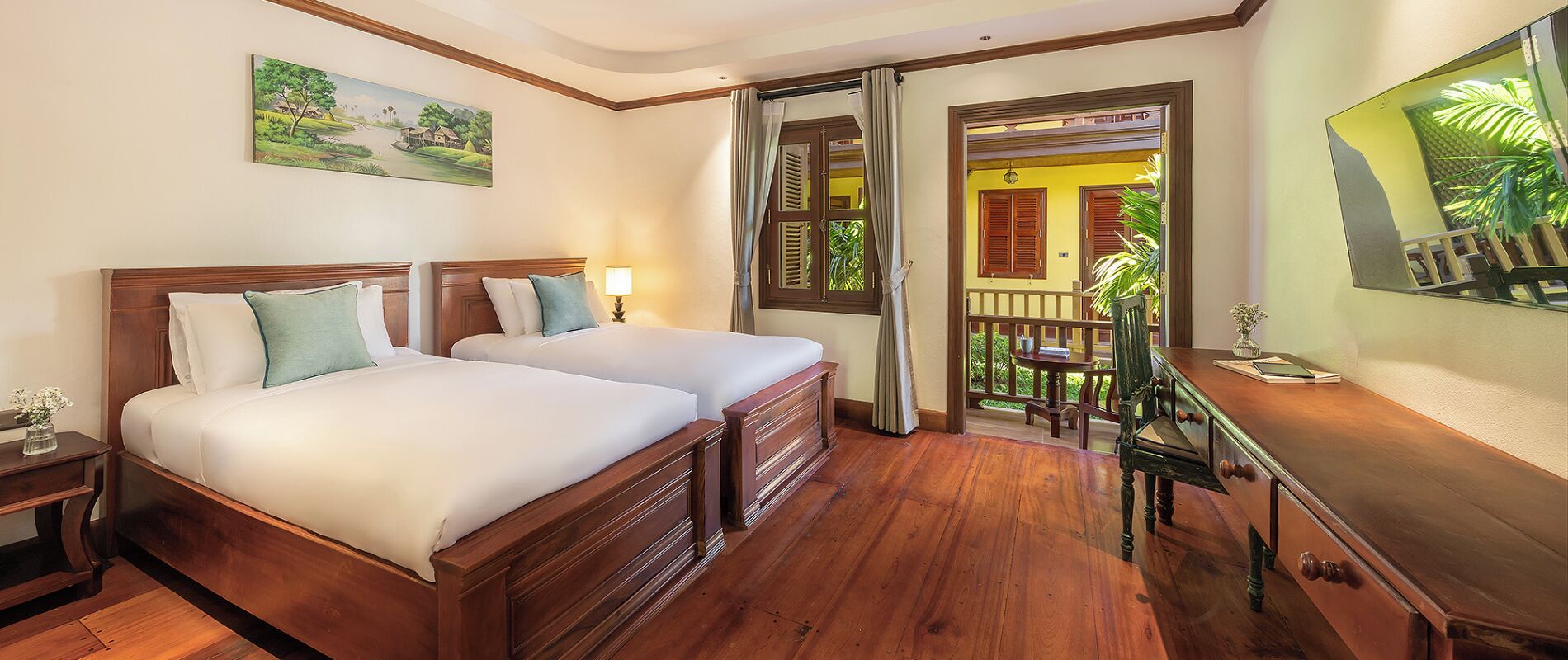 A hotel room with two wooden beds, a desk, a chair, and a view of the outside balcony.