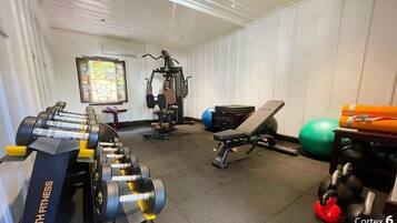 Un gimnasio con equipos de ejercicio variados, incluyendo mancuernas, una banca y una máquina de remo.