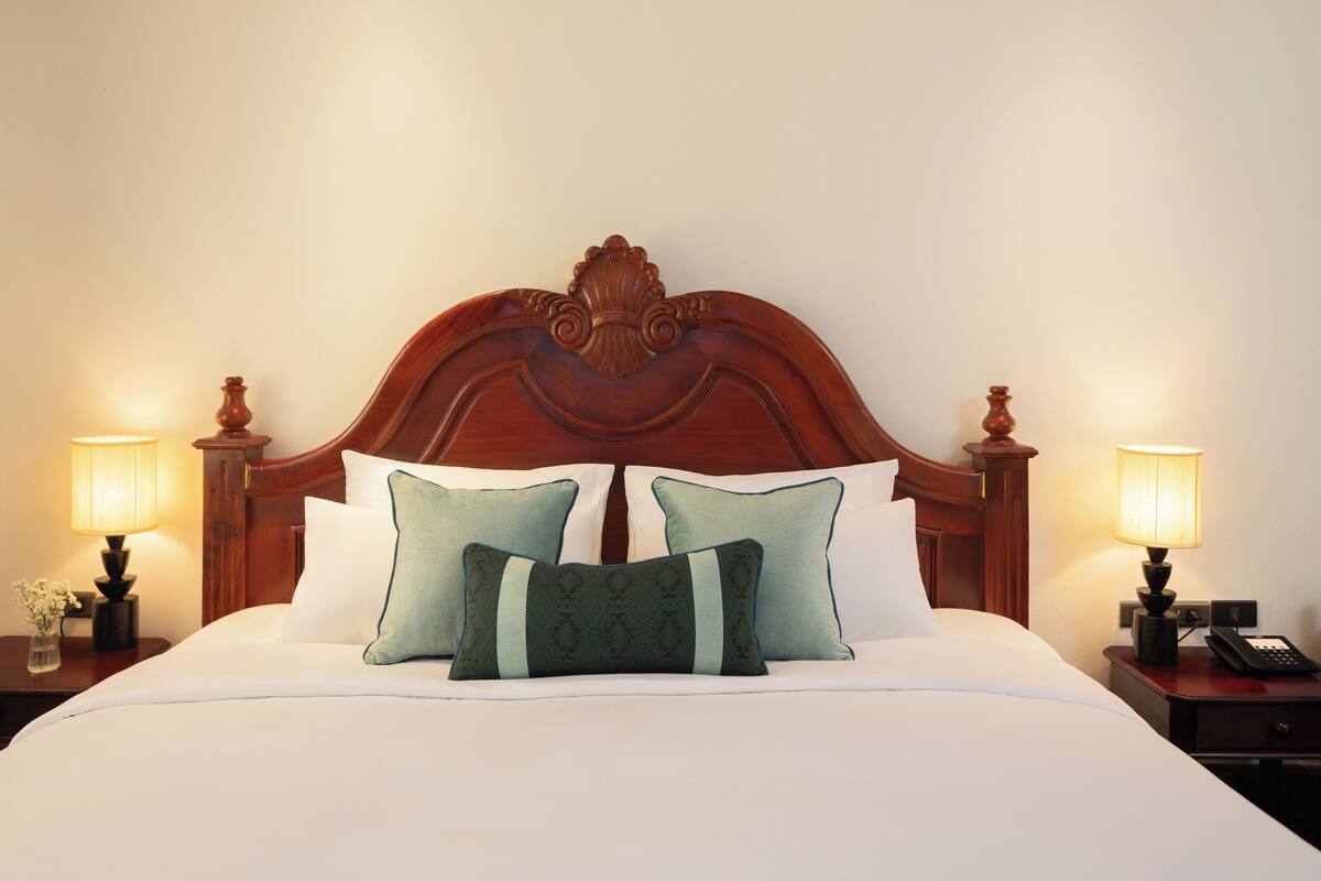 Una cama bien hecha con cabecera de madera, dos lámparas de noche y una mesita con un teléfono.