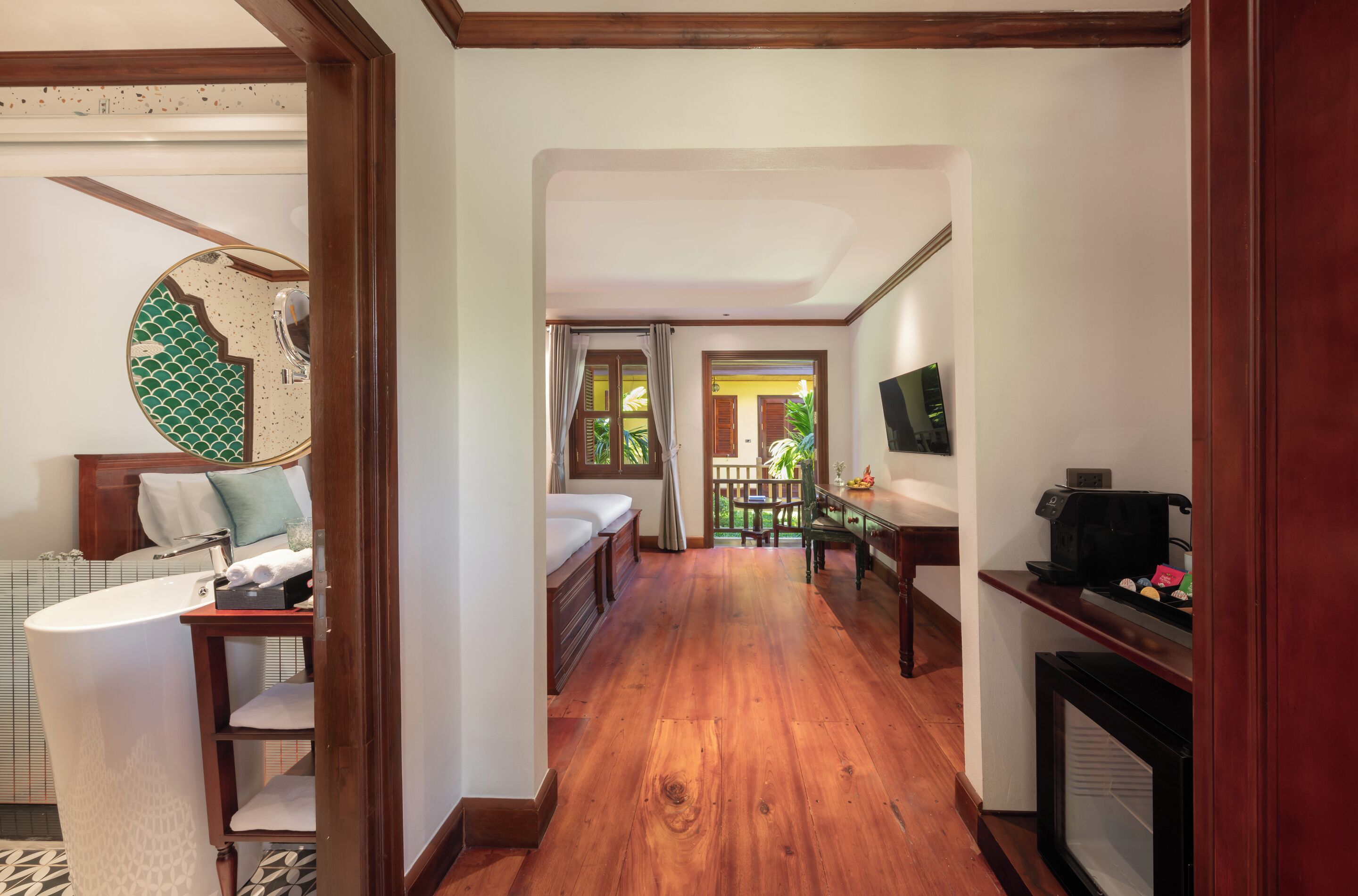 A hallway with a wooden floor, a bed, a desk, and a TV on the wall.