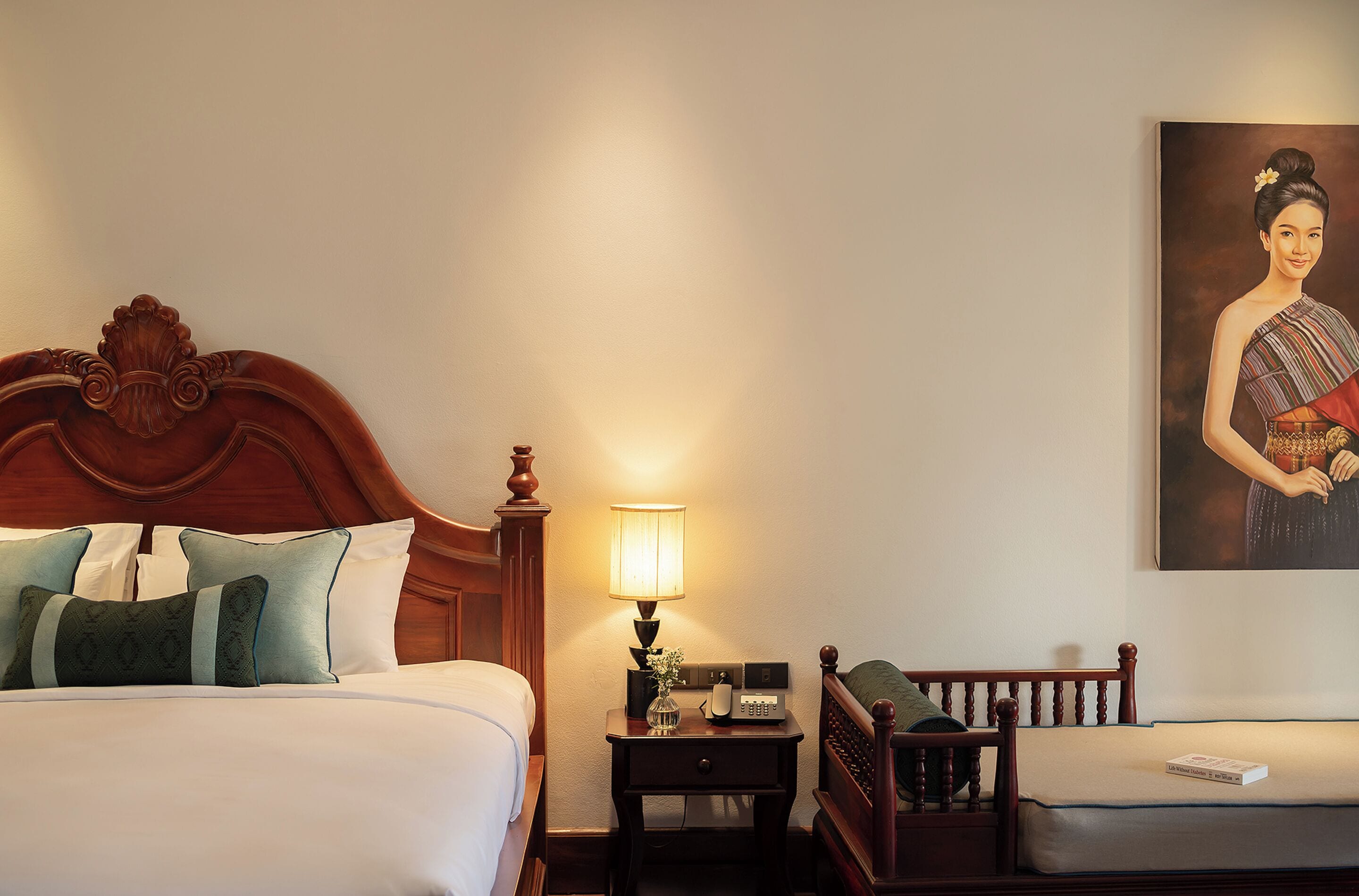 A hotel room with a large bed, a nightstand with a lamp, a small table, and a wall-mounted painting.