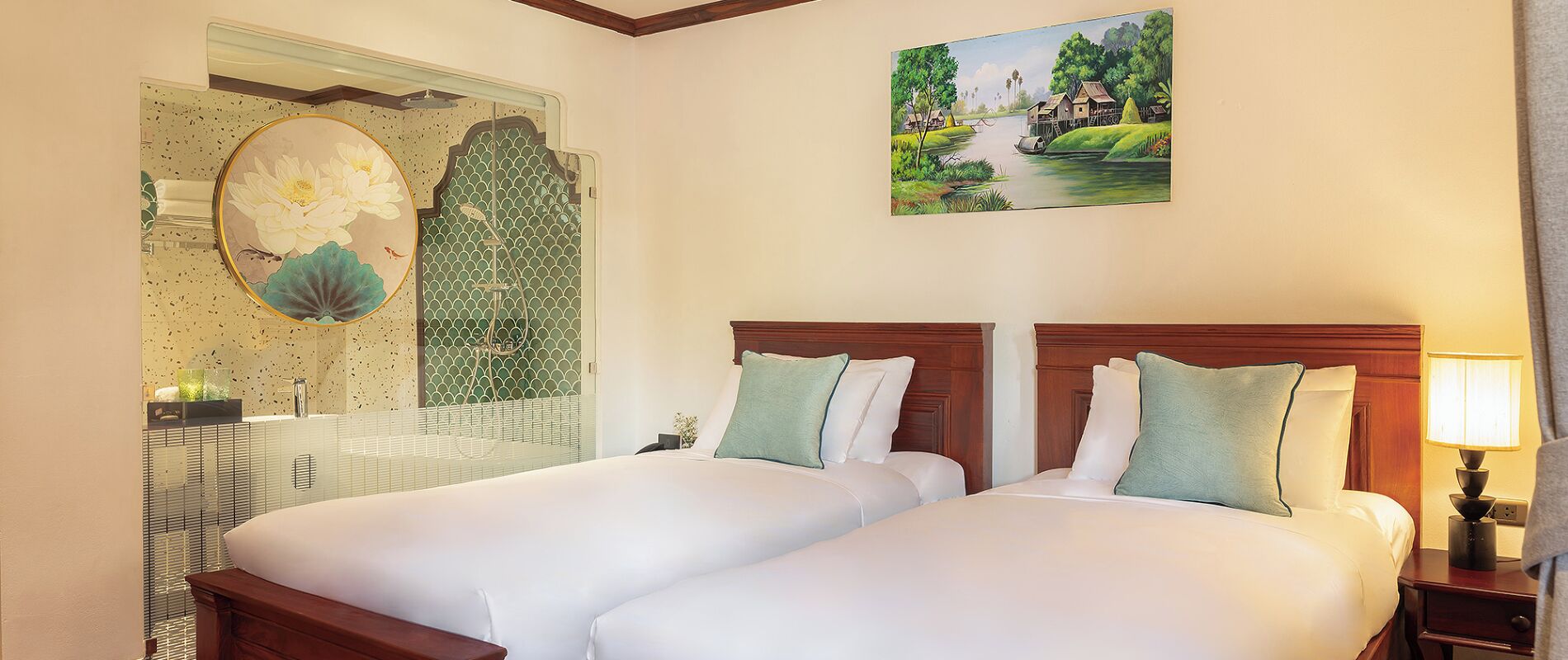 A hotel room with two beds, a painting on the wall, and a bathroom with a decorative mirror.