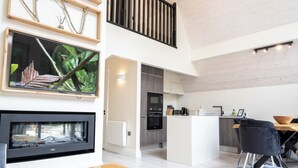 Ein modernes Wohnzimmer mit Kamin, einem großen Flachbildfernseher, einem Holztisch und einem Essbereich mit Holztisch und schwarzen Stühlen.