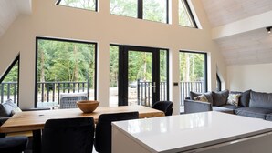 Ein modernes Interieur mit Essbereich, einer Couch und großen Fenstern, die Blick auf ein bewaldetes Gebiet bieten.