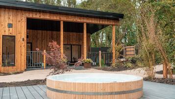 A wooden cabin with a covered porch, a hot tub, and a deck.