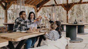 Eine Familie isst Pizza und Wein an einem Holztisch im Freien.