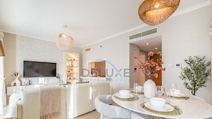 A modern, well-lit living room with a flat-screen TV, a sofa, a dining table set for four, and a kitchen area with a buffet. - Chic Studio in Burj Views Podium, Downtown Dubai by Deluxe Holiday Homes (Dubai)