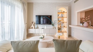 A modern living room with a flat-screen TV, a white coffee table, and a bookshelf with decorative items. - Chic Studio in Burj Views Podium, Downtown Dubai by Deluxe Holiday Homes (Dubai)