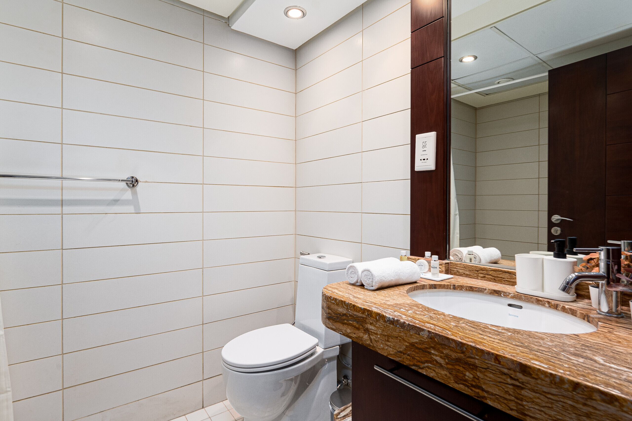 Un baño moderno con baldosas blancas, lavamanos de mármol y un espejo grande.