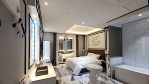 A modern hotel room with a large bed, a vanity with a mirror, a desk, and a bathroom with a bathtub. - VIVID (Muan)