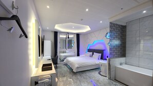A modern hotel room with a bed, a desk with a computer, a bathroom with a bathtub, and a mirror. - VIVID (Muan)