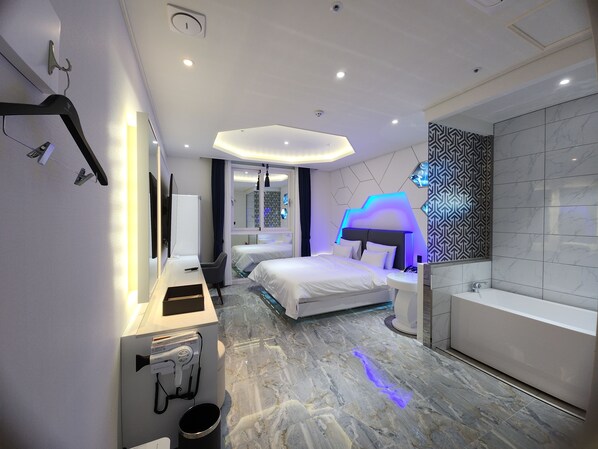Una habitación de hotel moderna con cama, escritorio con computadora, baño con bañera y espejo.