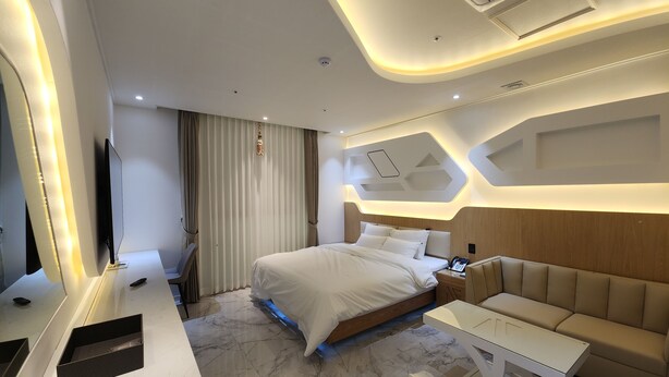 A modern hotel room with a large bed, a sofa, a desk, and a TV. - VIVID (Muan)