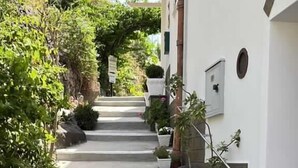 Una escalera de concreto estrecha que sube hacia un edificio blanco con plantas en macetas a los lados.