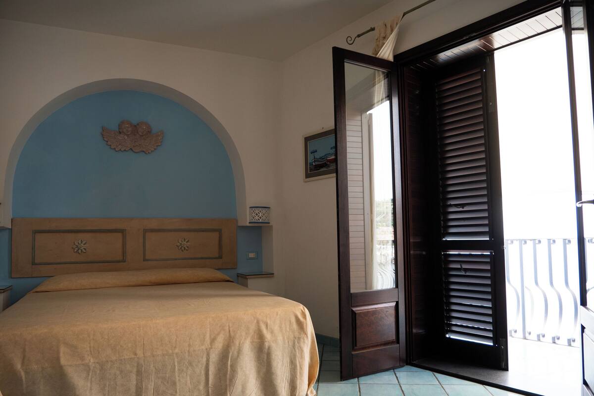 A bedroom with a bed, a nightstand, a wall-mounted decorative piece, and a door leading to a balcony.