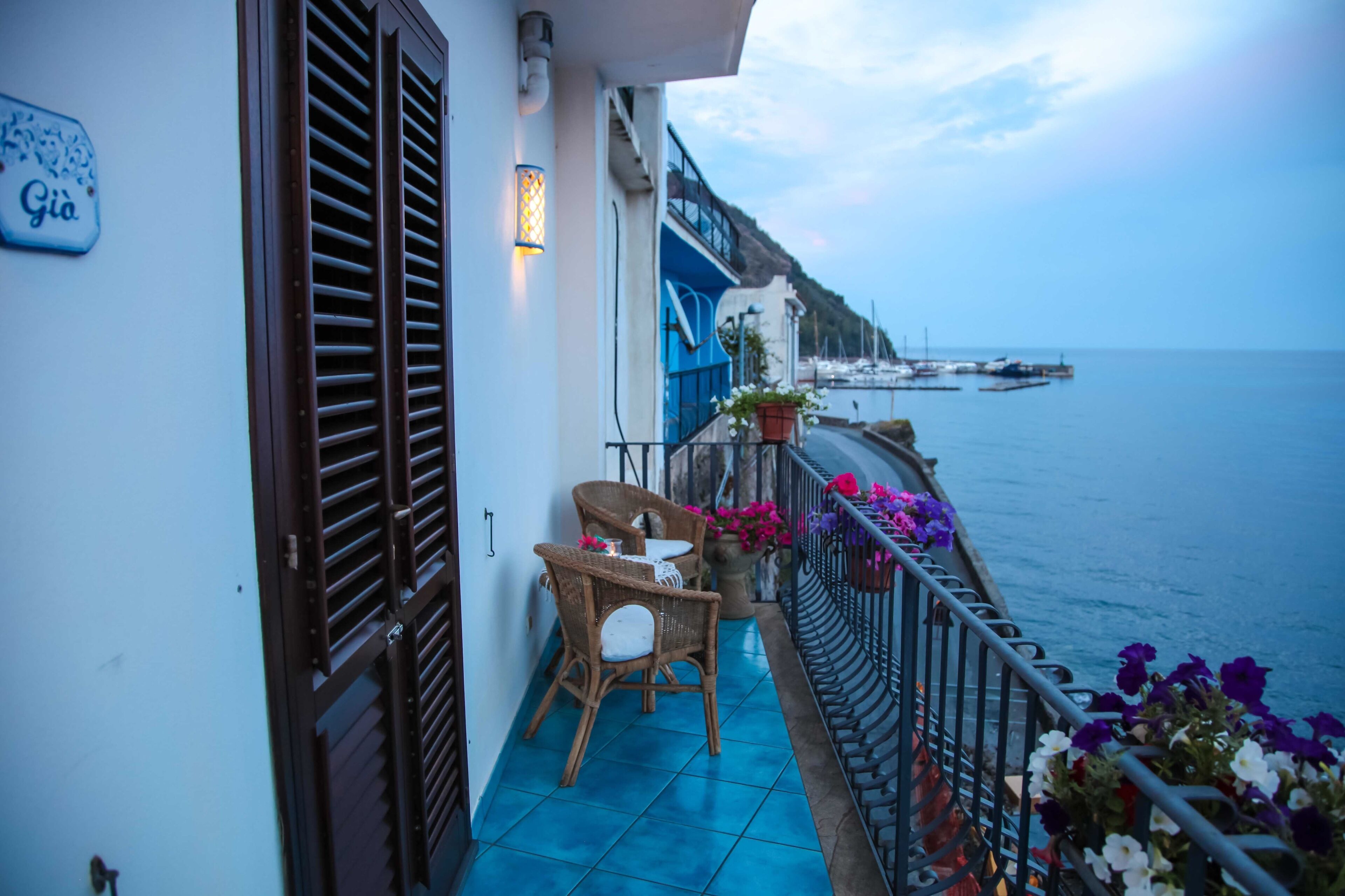 Un balcon avec des fauteuils en osier et une table, donnant sur une marina où sont amarrés des bateaux.