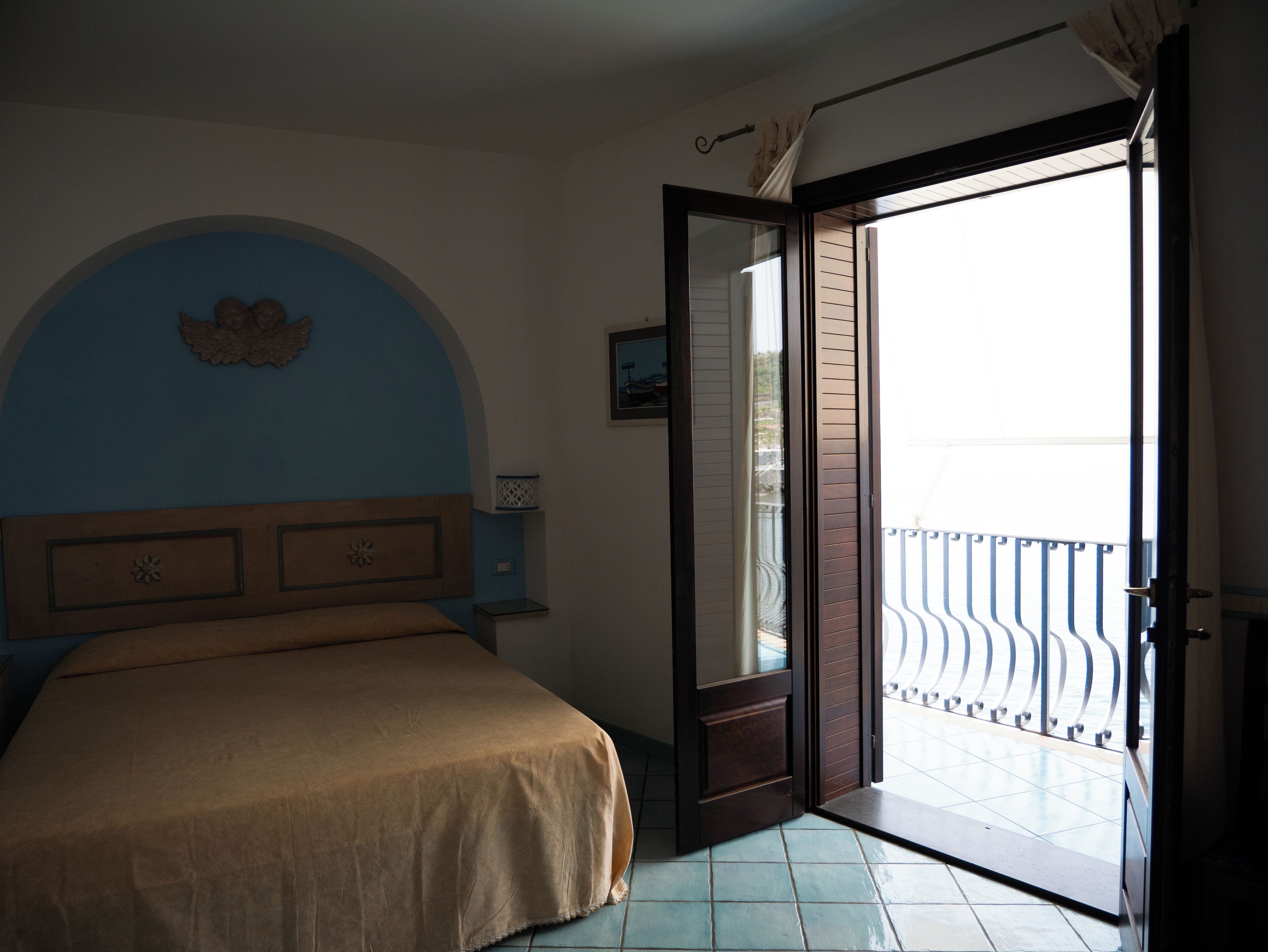 Un dormitorio con cama, mesita de noche, lámpara de pared y balcón con barandilla.