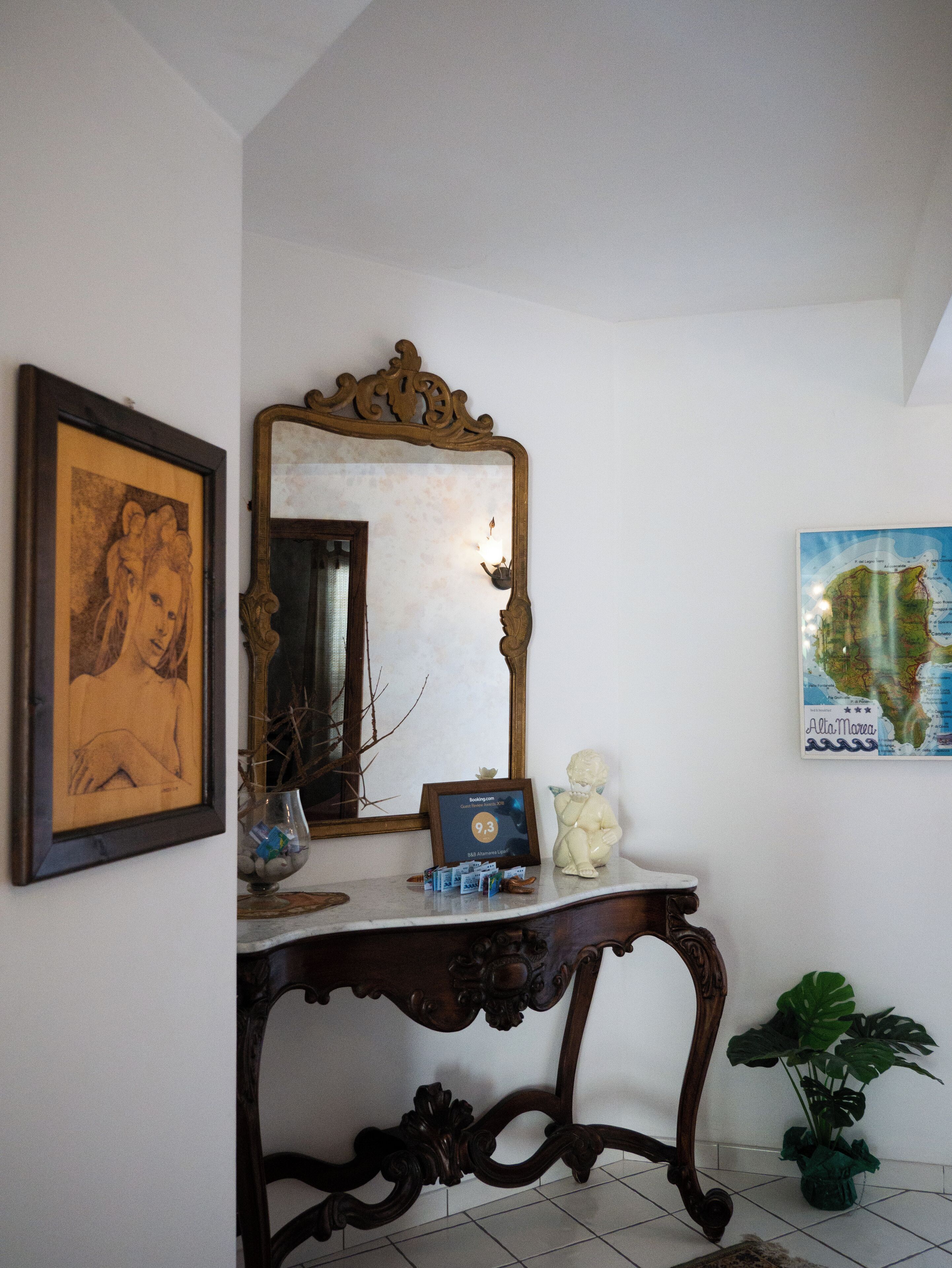 A room with a large ornate mirror, a framed artwork, a decorative table, and a map on the wall.