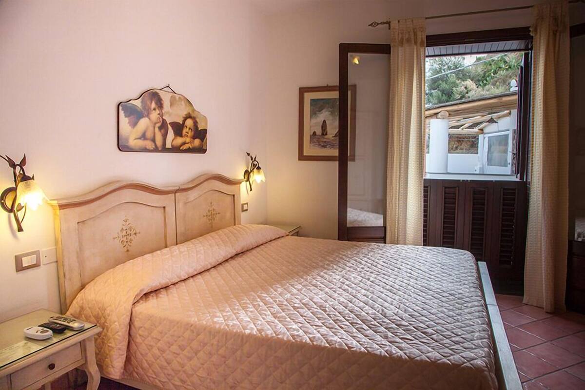 A bedroom with a bed, bedside lamps, a nightstand, a painting on the wall, and a window with curtains.