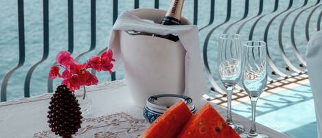 A table with a bottle of champagne, two glasses, a plate with watermelon slices, and a vase with flowers.