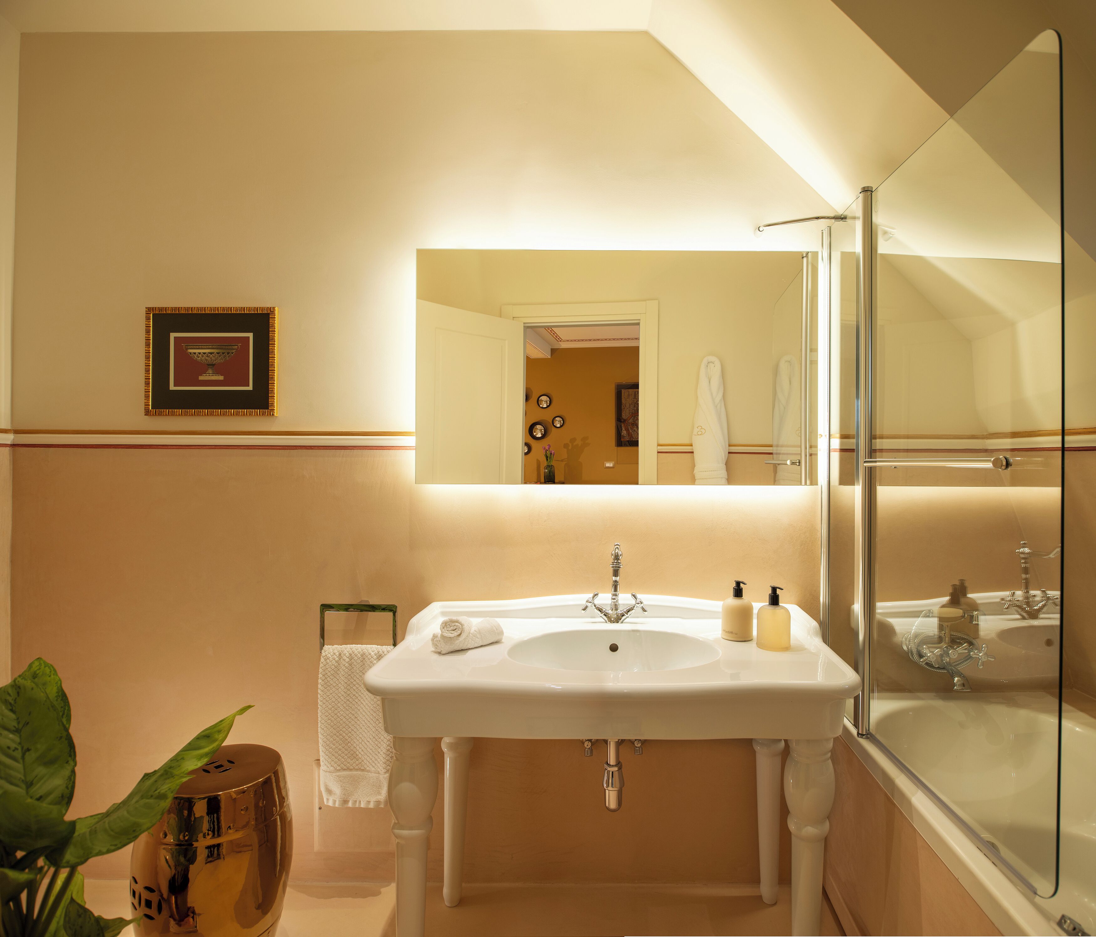 Un bagno con un lavandino bianco, cabina doccia in vetro e un quadro appeso al muro.