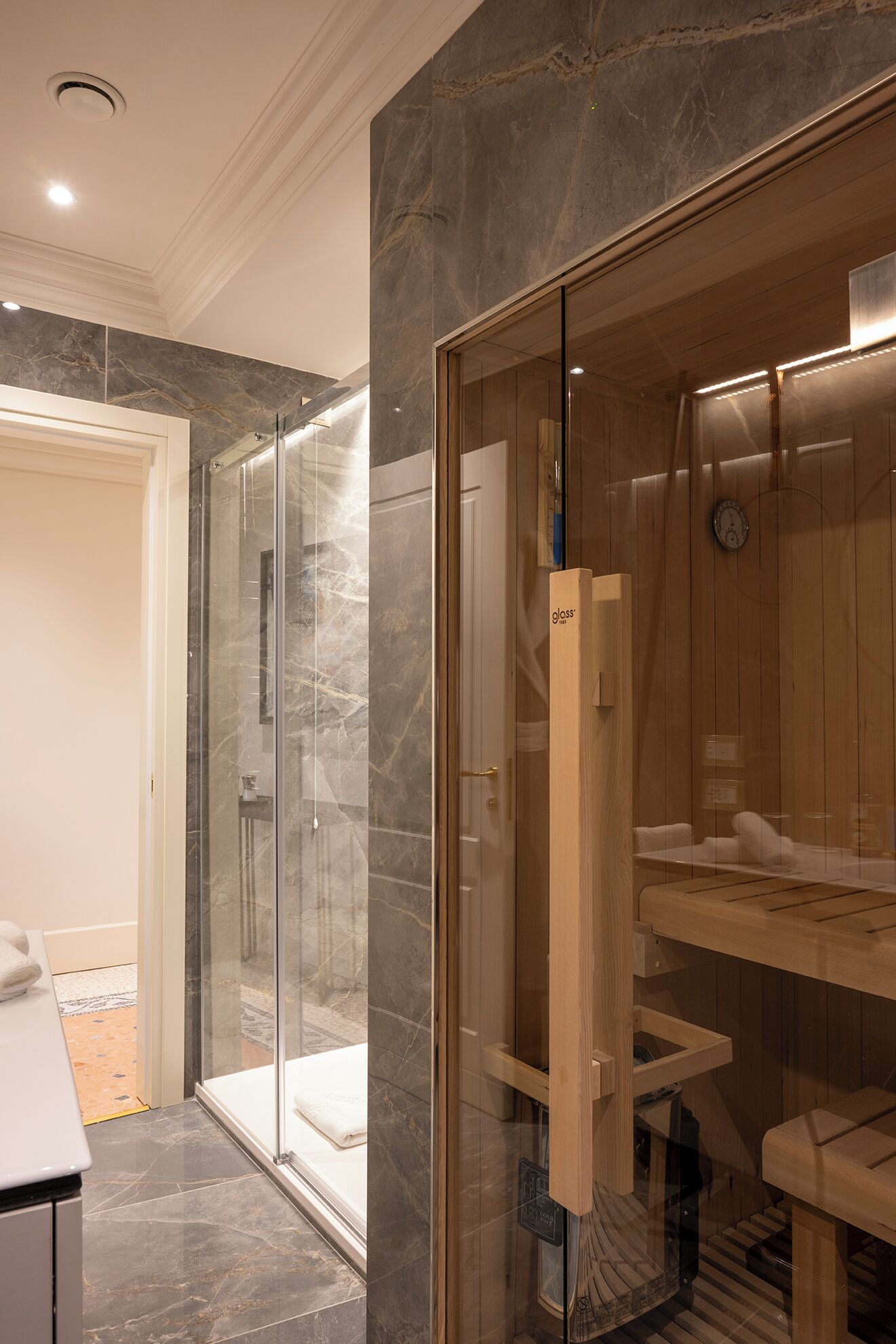 Un baño moderno con ducha envuelta en vidrio, sauna de madera y suelo de mármol.
