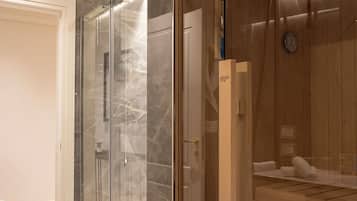 Un baño moderno con ducha envuelta en vidrio, sauna de madera y suelo de mármol.