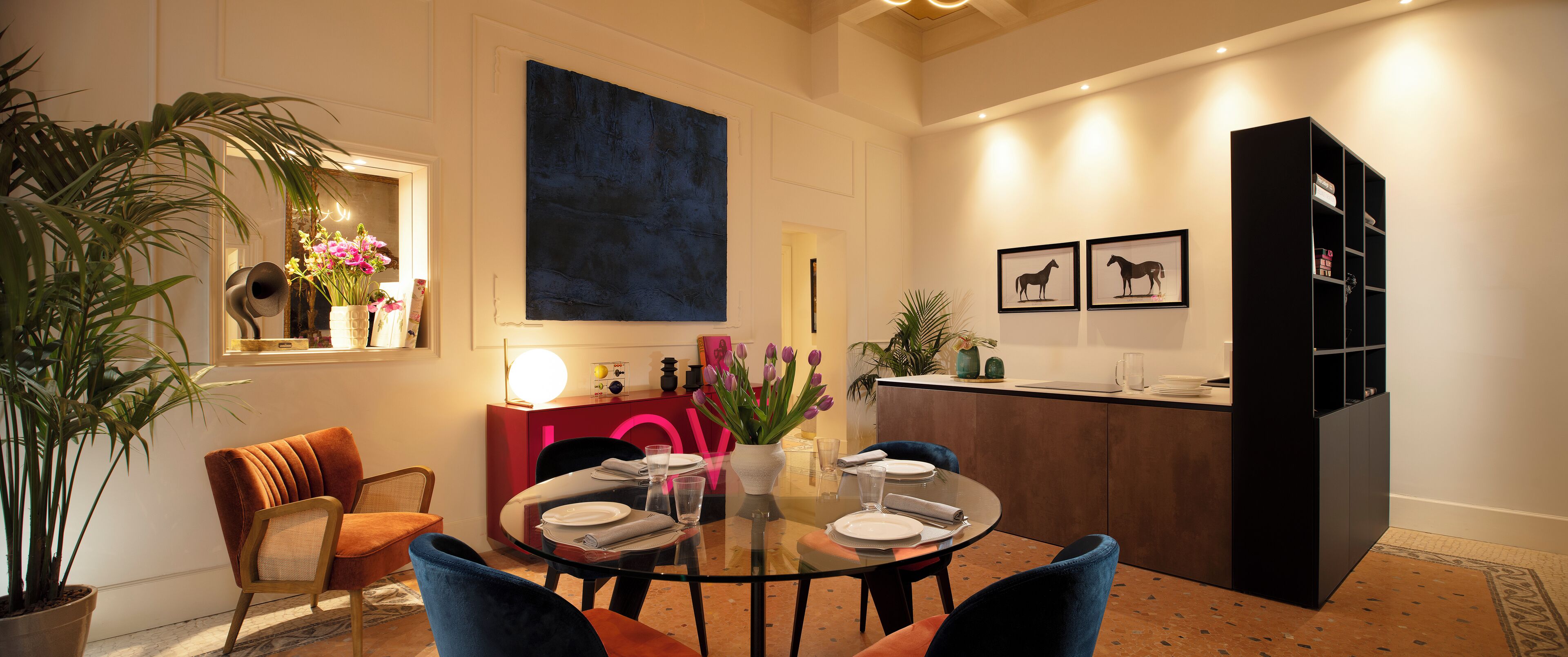 Un comedor moderno con una mesa de vidrio, sillas acolchadas y una pared de acento roja.