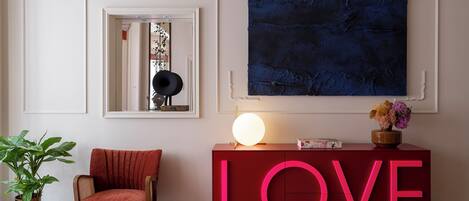 Una habitación con un letrero rojo que dice LOVE, un cuadro azul oscuro grande, una silla roja, una planta en maceta y un piso con diseño de mosaico.