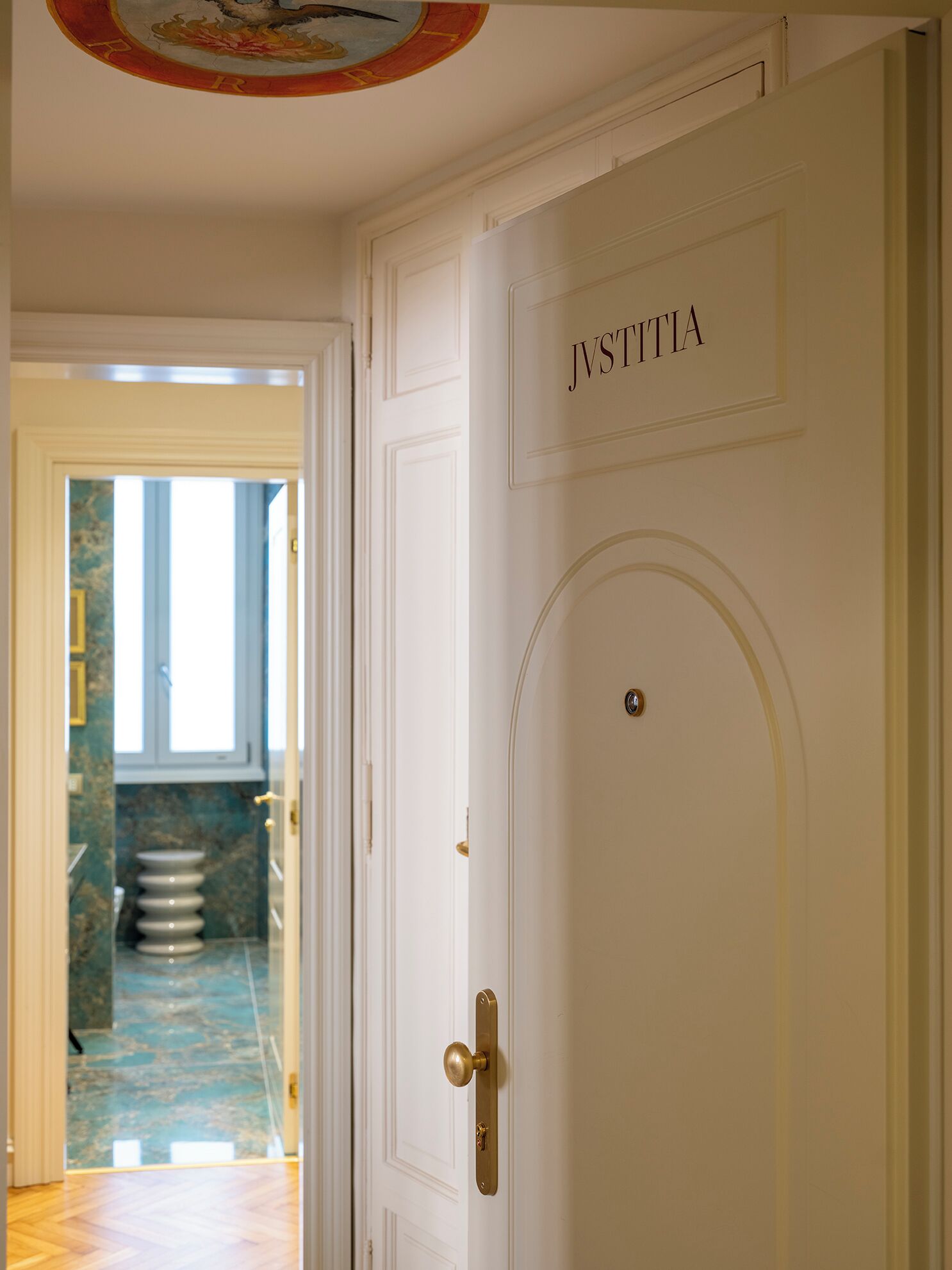 Una puerta blanca con el nombre "JSTITTA" encima, que da a un pasillo con suelo de mármol y una escalera.