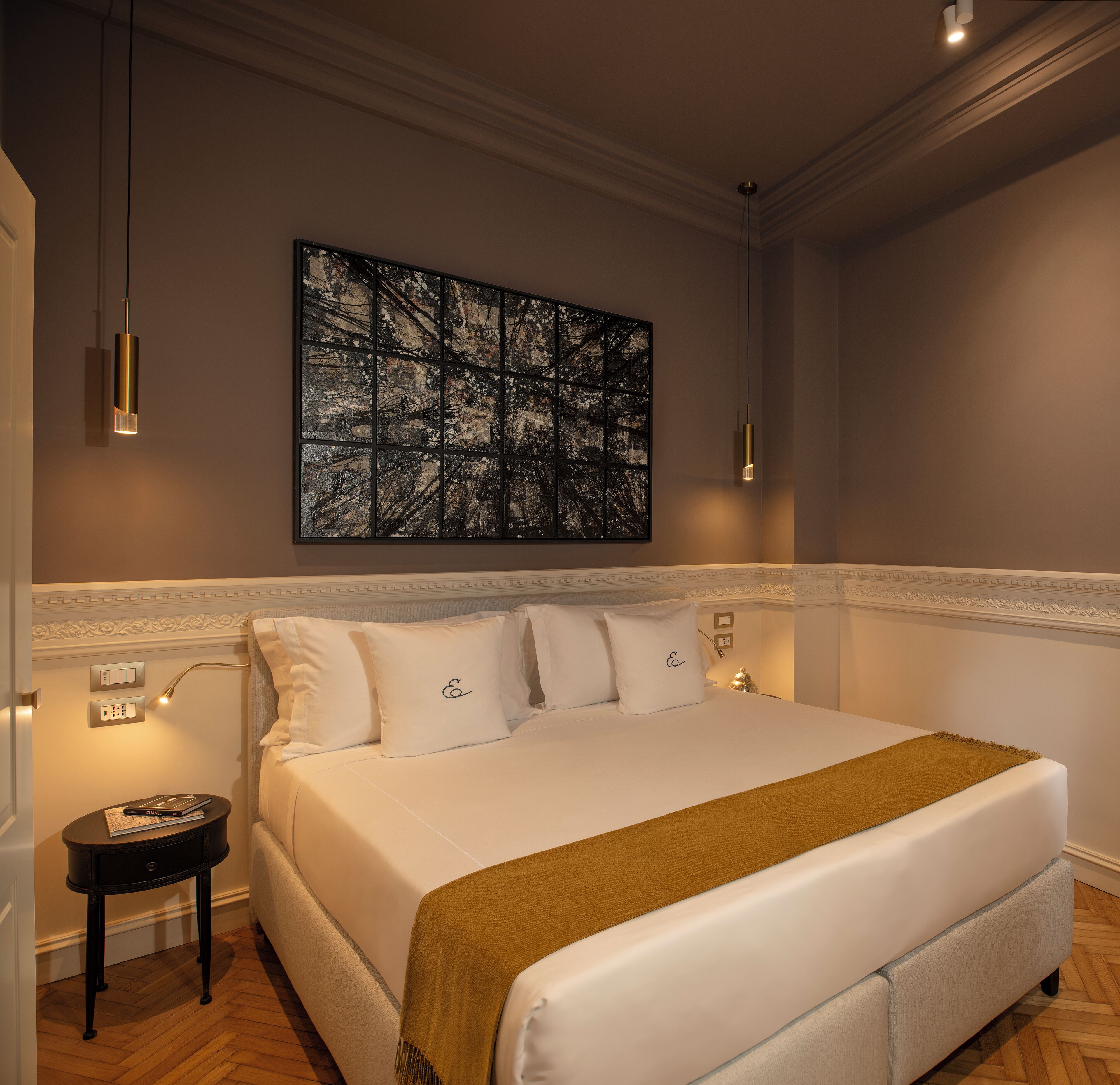 Une chambre d’hôtel avec un grand lit, une table de chevet, une œuvre d’art accrochée au mur et un luminaire suspendu.
