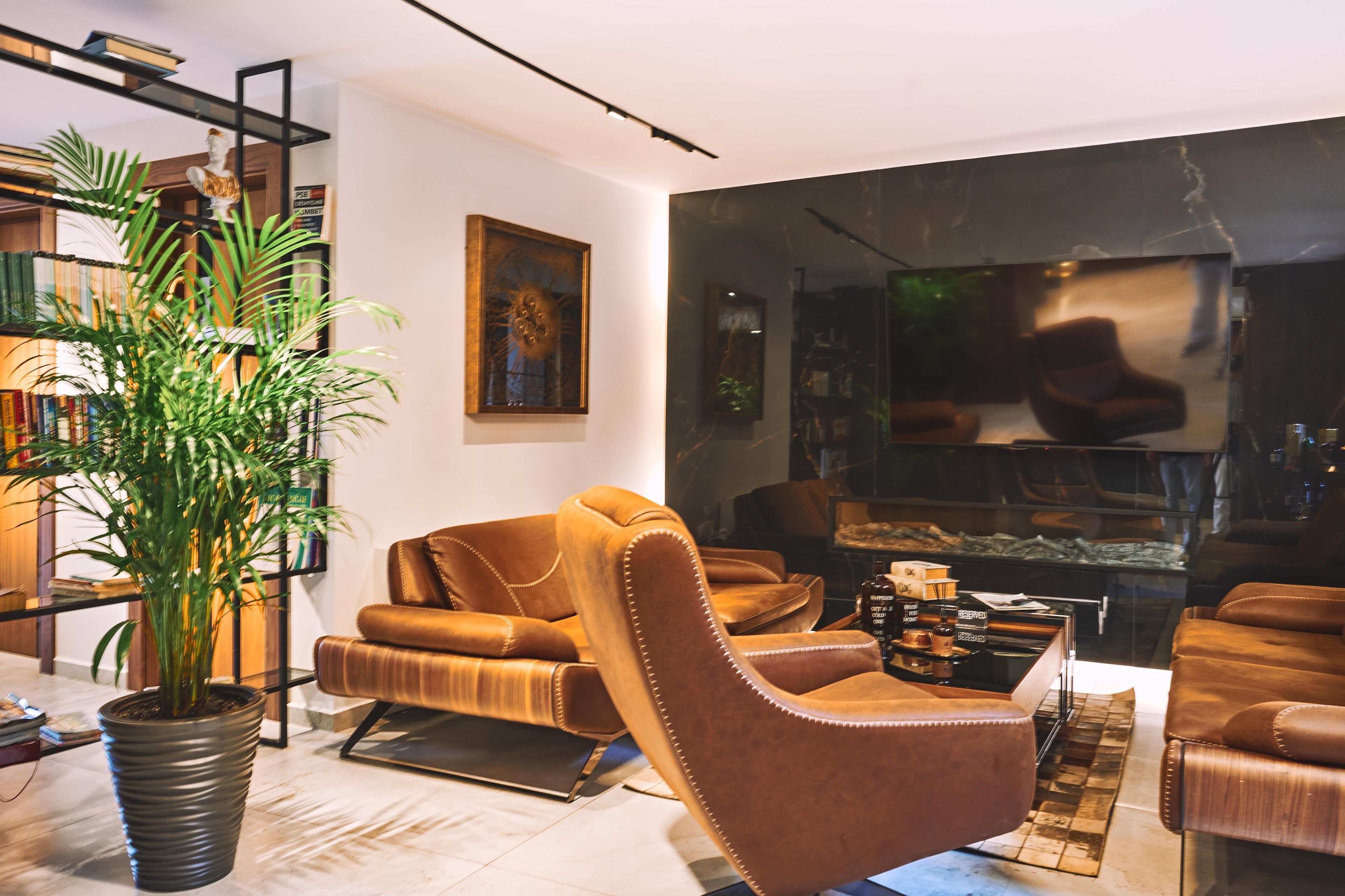 Een moderne woonkamer met een grote potplant, leren fauteuils, een boekenkast en een open haard.
