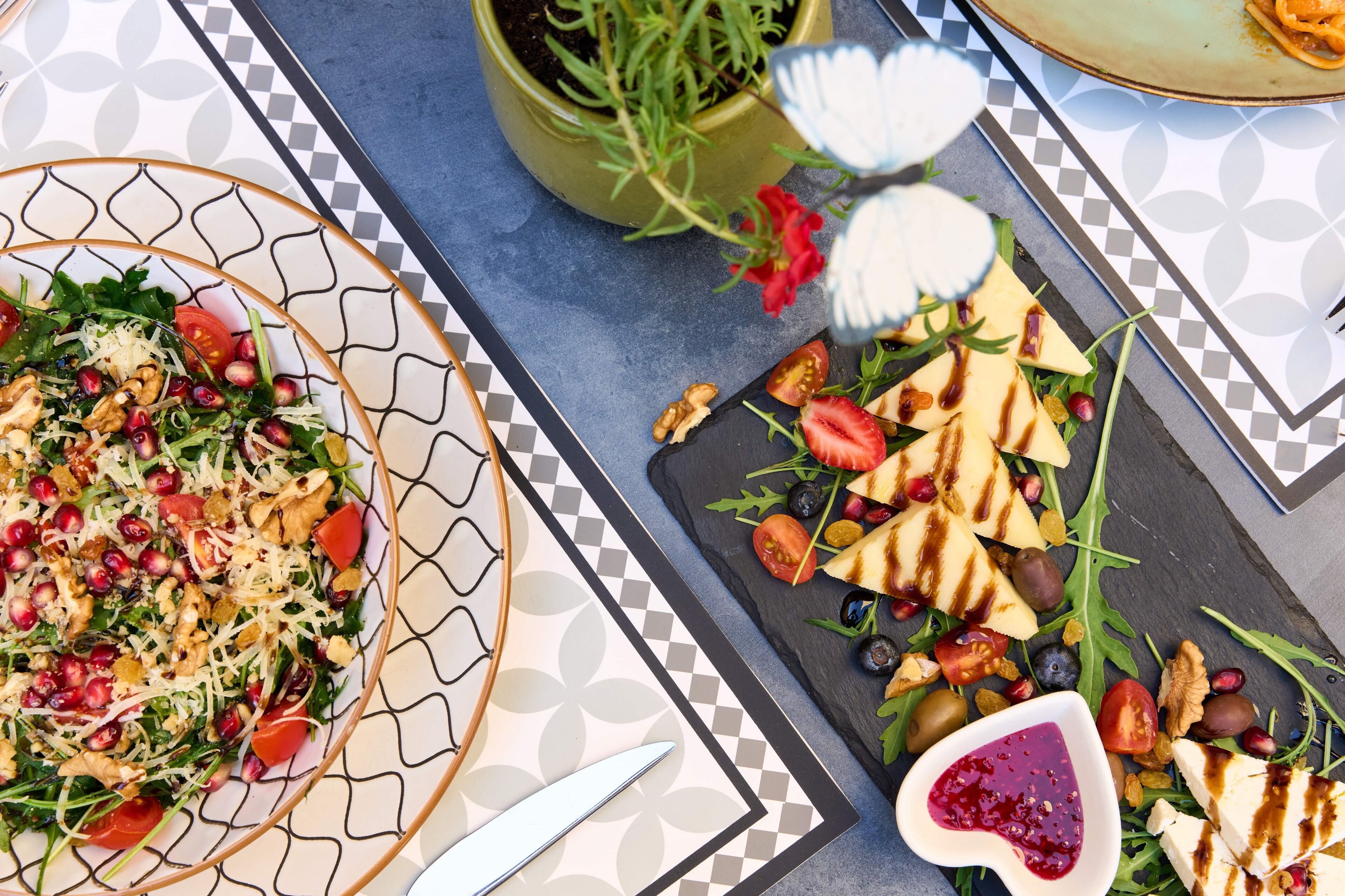 A table with a variety of food items including a salad, grilled cheese, and a bowl of jam.