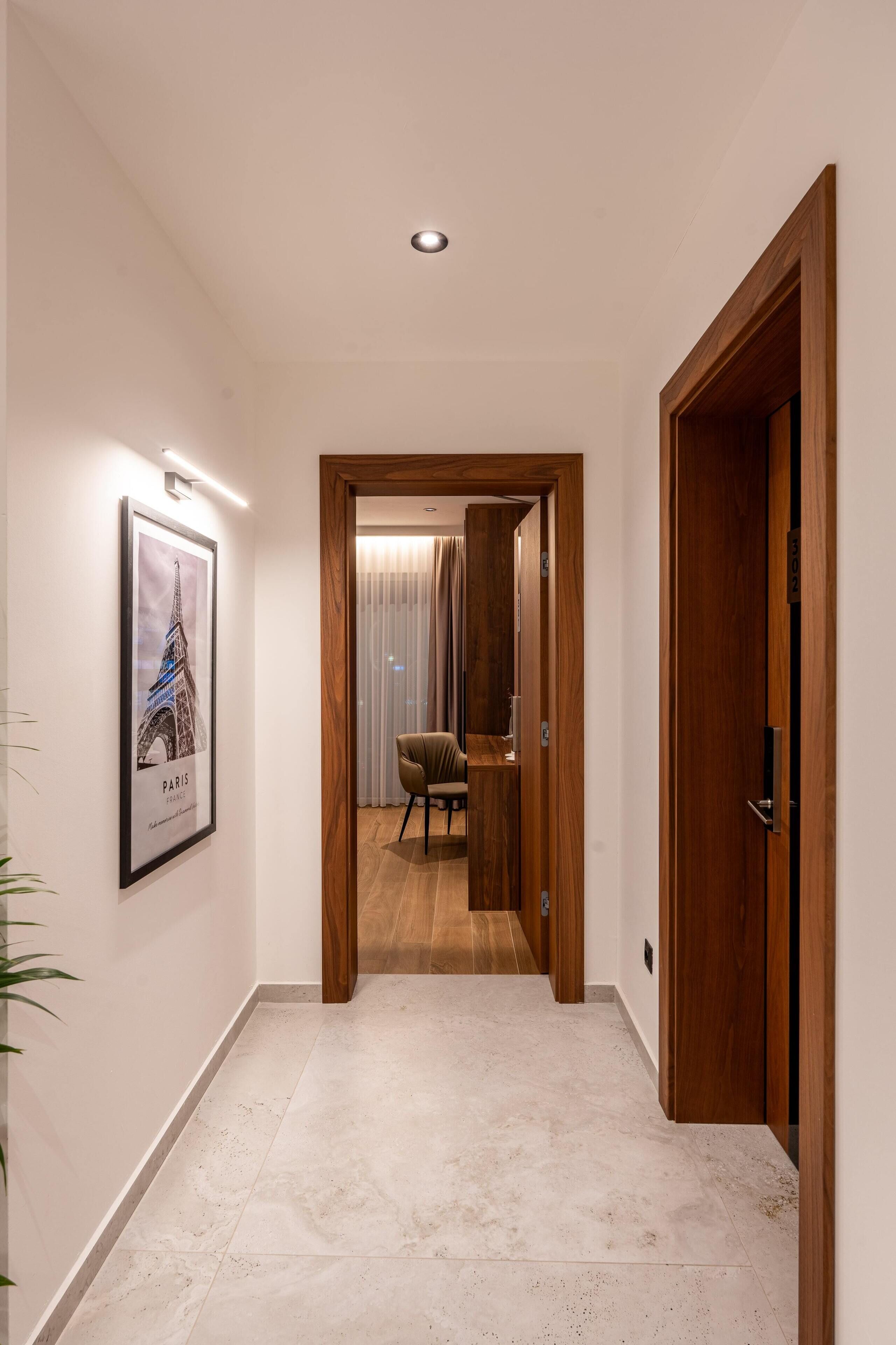 Un couloir avec un tableau encadré représentant la Tour Eiffel, une porte en bois et une chaise au fond.