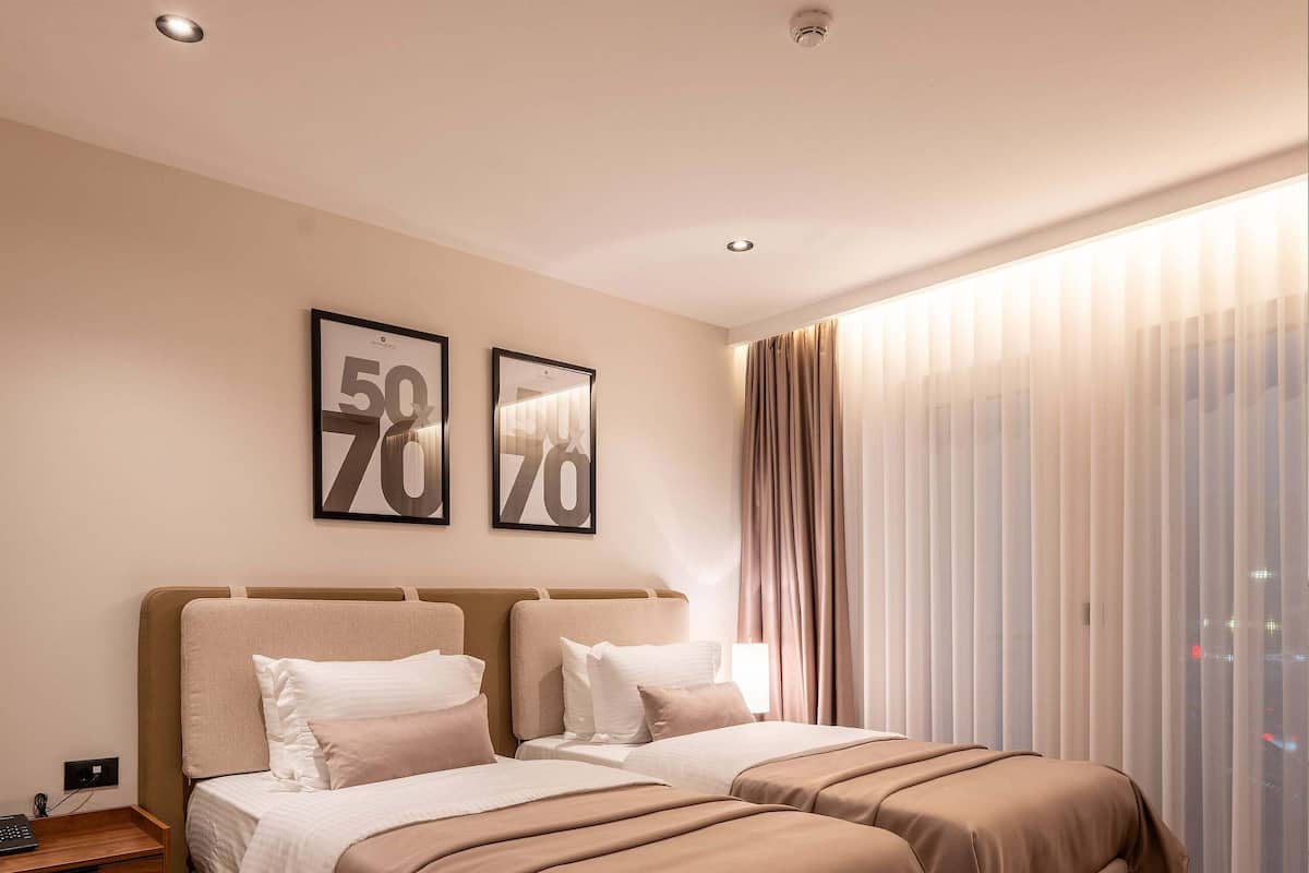A double bed with a headboard, a bedside table, and a window with sheer curtains.