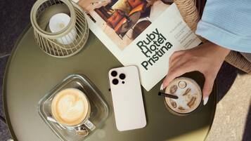 Un tavolo con una tazza da caffè in vetro, uno smartphone, una candela e un menu dell'Hotel Ruby Pristina.