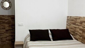 A bed with a striped bedspread, two black pillows, a nightstand, a wall-mounted mirror, and a textured wall. - Apartamento Caleta Beach (Cádiz)