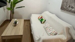 A small room with a bed, a table, a plant, and a wall-mounted air conditioner. - Apartamento Caleta Beach (Cádiz)