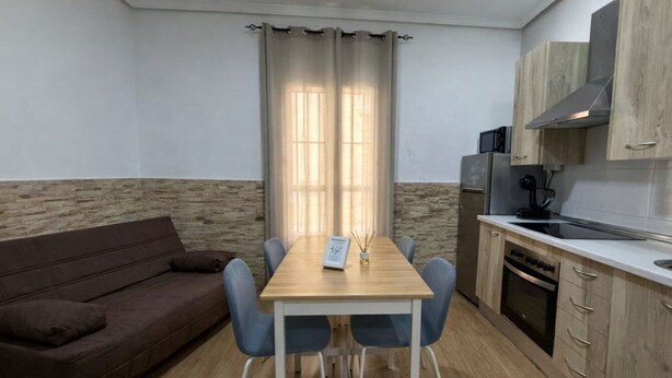 A compact kitchen with a dining table, chairs, a sofa, and a microwave. - Apartamento Caleta Beach (Cádiz)