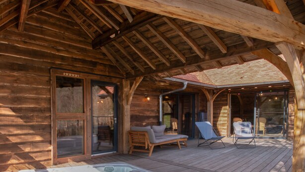 Una cabaña de madera con jacuzzi, terraza de madera y zona de estar al aire libre.