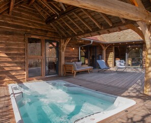 Eine Holzblockhütte mit Whirlpool, einer Holzterrasse und einer Sitzgelegenheit im Freien.