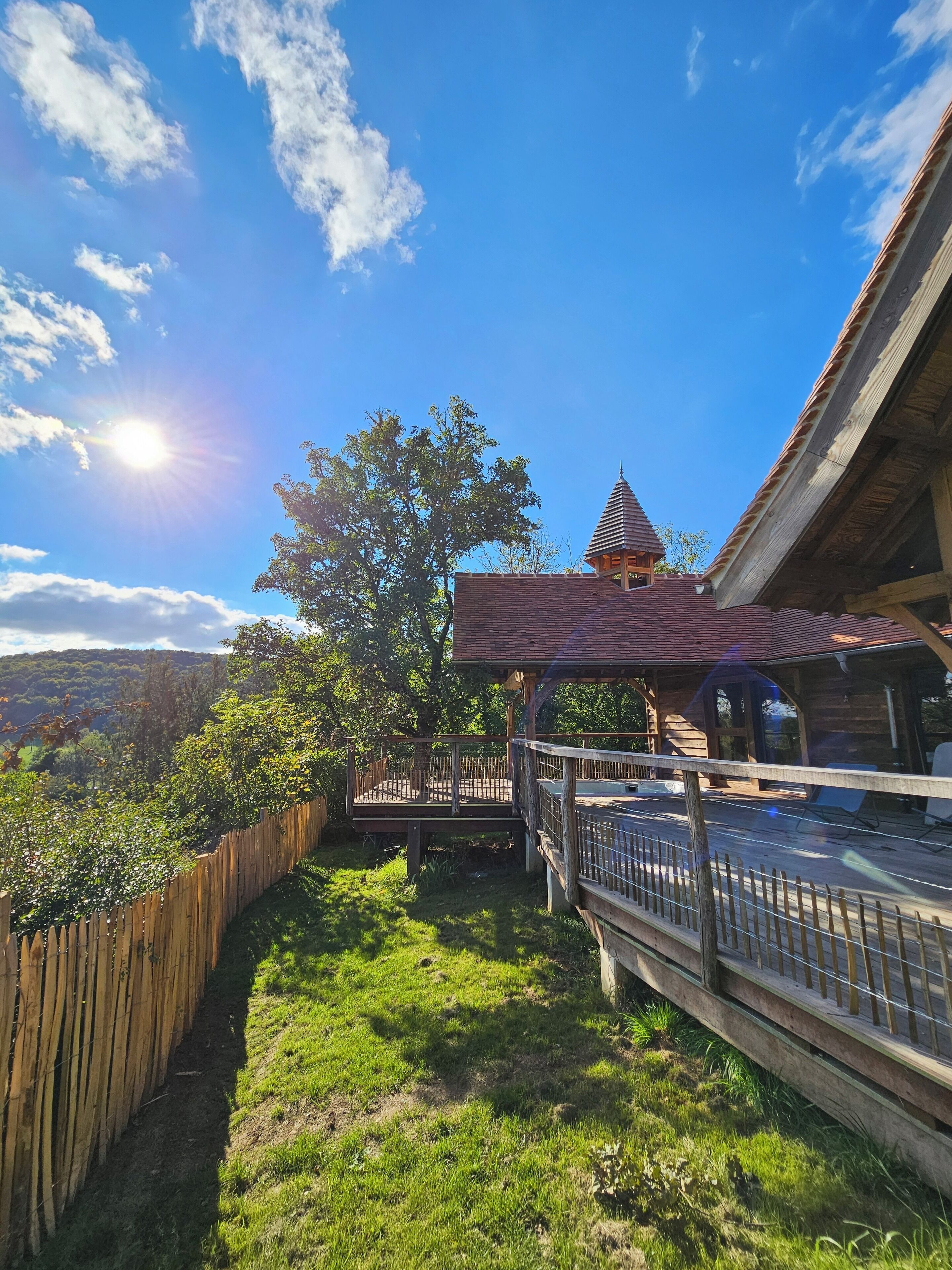 A wooden cabin with a balcony, surrounded by a wooden fence and a view of the landscape.