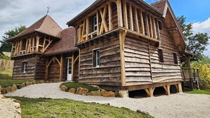Una casa de madera tradicional con techo a dos aguas pronunciado, chimenea visible y camino de grava que lleva a la entrada.