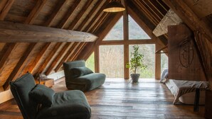 Un cuarto ático acogedor con techo inclinado, vigas de madera, un ventanal grande y una planta en maceta.