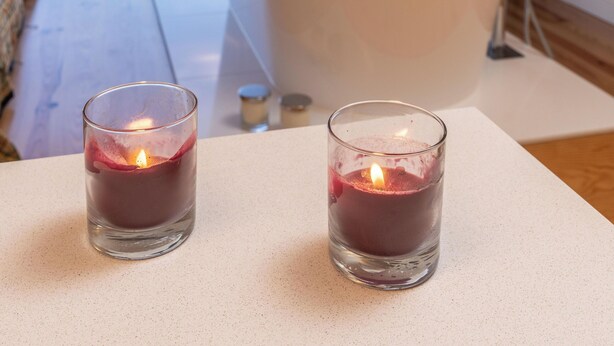 Een moderne badkamer met een vrijstaand bad, een groot raam met uitzicht op zee en twee brandende kaarsen op een tafel.